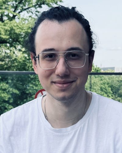 Der Geschäftsführer von OMNI2, Eugen Günter, lächelt in die Kamera. Er trägt eine Brille, ein weißes Shirt und hat seine Haare gebunden.